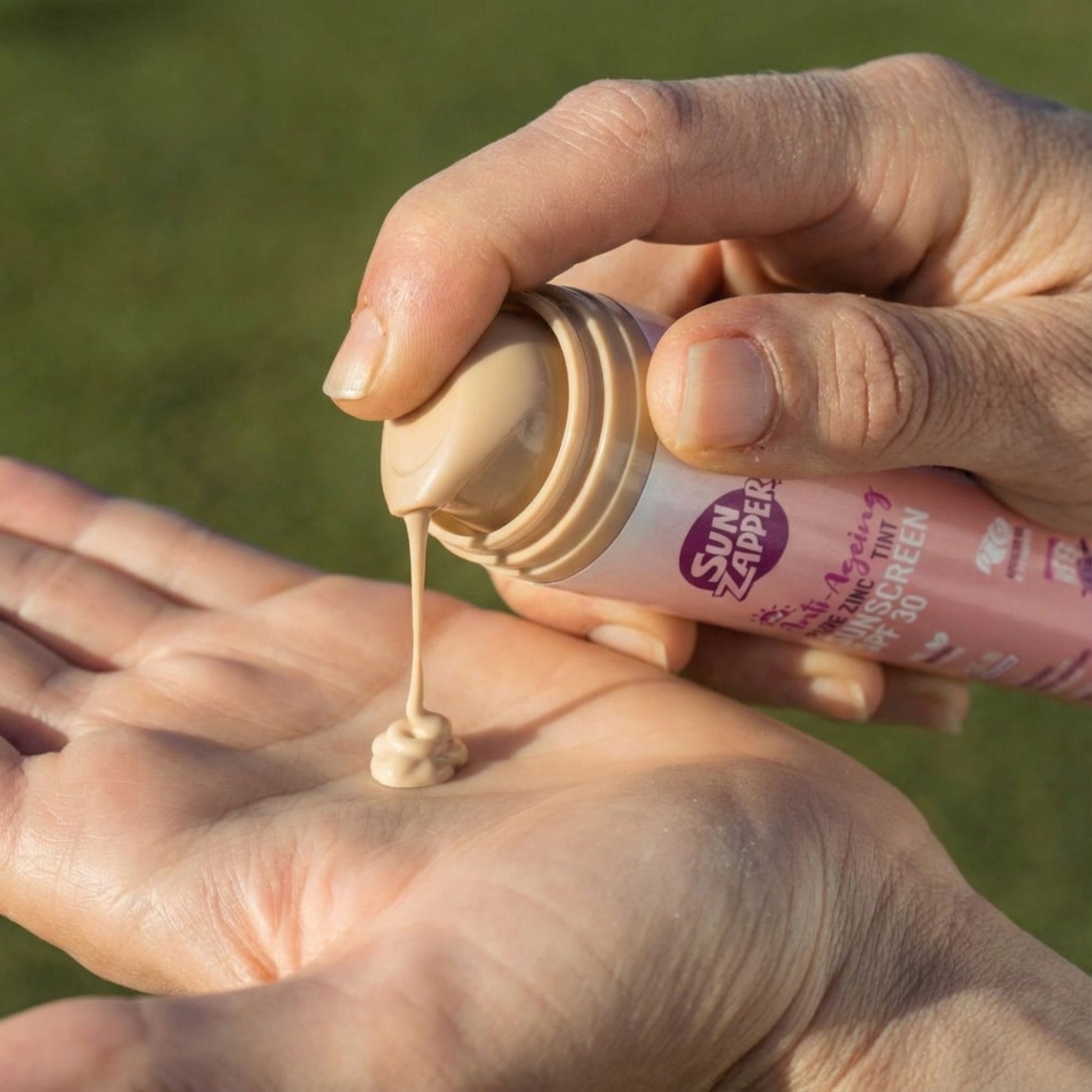 Person applying sunscreen cream from a bottle onto their palm with a green outdoor background