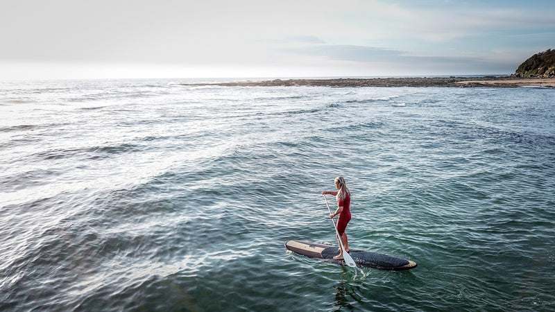 Person paddleboarding on a calm ocean with a clear sky 